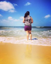 Rear view of woman standing on shore at beach against sky