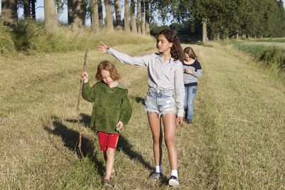 Rear view of friends walking on grassland against trees