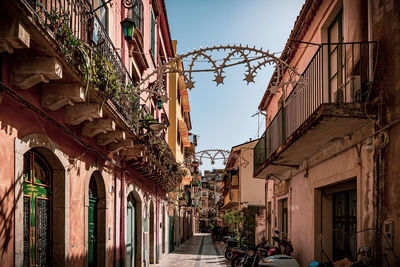 Narrow cobble lane between red wall buildings with balconies and potted plants in taormina, sicily