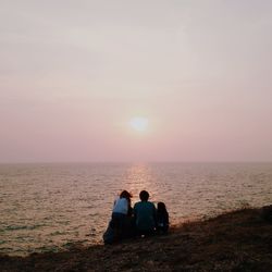 Rear view of women sitting on shore against sunset sky