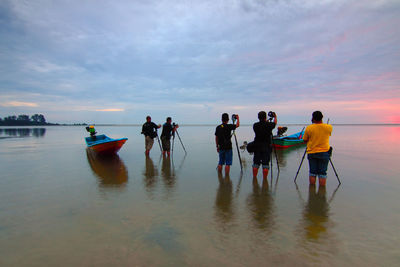 People at beach against sky during sunset