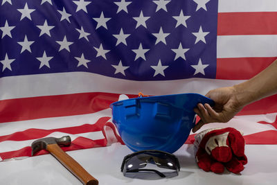 Cropped hand of person holding hardhat by work tools and american flag
