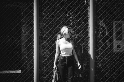 Young woman standing against chainlink fence