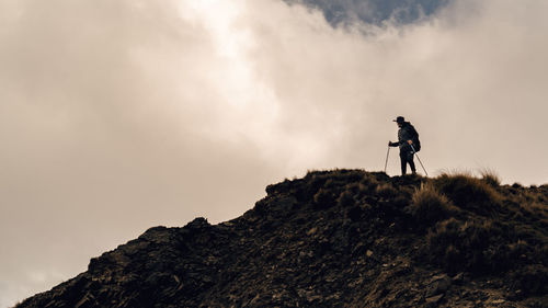 Low angle view of man hiking on mountain against cloudy sky