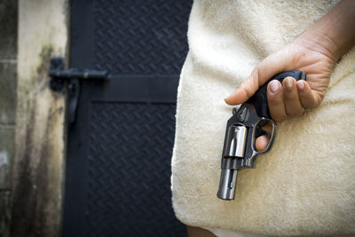 Rear view of woman holding handgun behind her back by gate