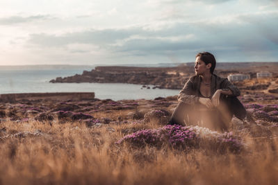 Young woman sitting on land against sky