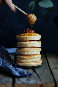Cropped hand pouring honey on pancakes stacked on table