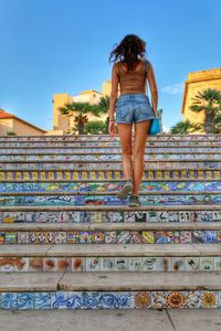 Low section of woman standing on staircase against blue sky