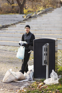 Portrait of environmentalist with plastic waste standing by garbage can