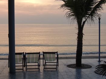 Chairs and table on beach against sky during sunset