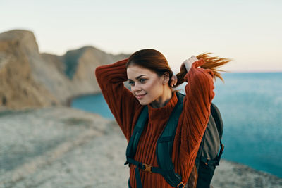 Smiling young woman standing at beach against sky