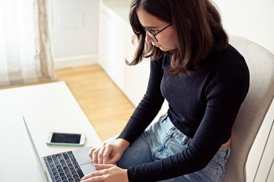 Midsection of woman using phone while sitting on table