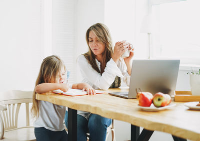 Working mom freelancer on laptop with little daughter drawing on table at home
