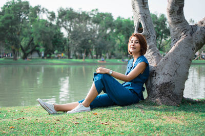 Portrait of woman sitting by tree trunk at riverbank