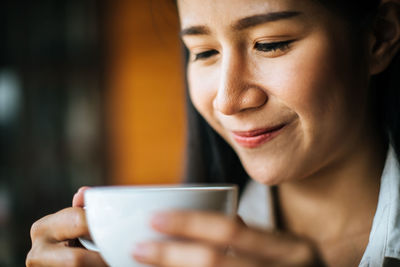 Close-up of smiling woman holding coffee cup while sitting in cafe