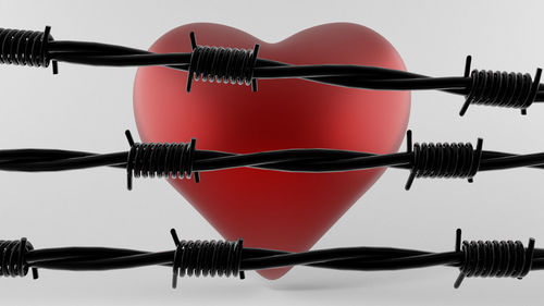 Close-up of heart shape and barbed wires against white background