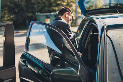 A young man stands near an open car door.