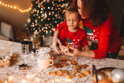 Parents and a child in red pajamas prepare christmas cookies in the decorated kitchen of the house