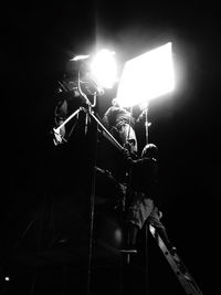 Low angle view of illuminated lighting equipment against black background