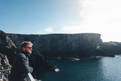 Young man wearing sunglasses standing on observation point against sky