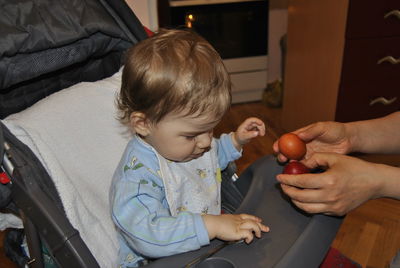 Cropped hands of showing eggs to son on baby stroller at home