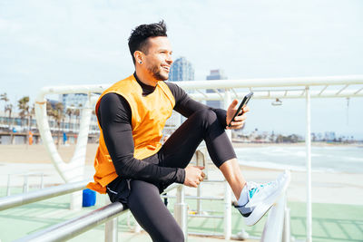 Smiling man with smart phone sitting on railing