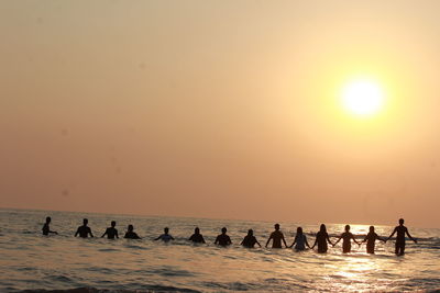 Silhouette people on beach against sky during sunset