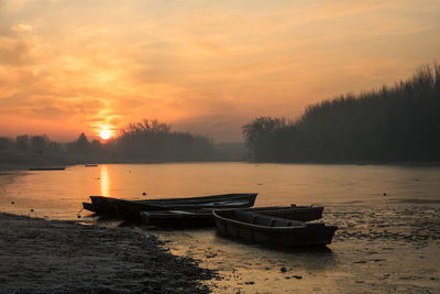 Boats moored on shore during sunset