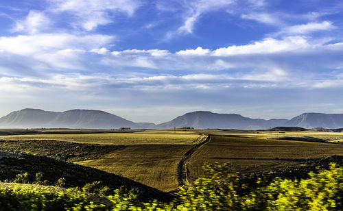 Scenic view of fields against sky, mountain range in the background 