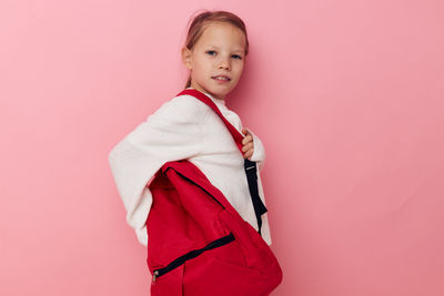 Portrait of cute girl with backpack against pink background