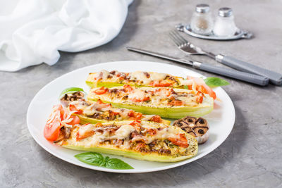 Ready-to-eat baked zucchini halves stuffed with cheese and tomato and basil leaves on a plate 