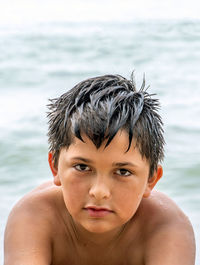 Handsome young boy poses for a close up as he sits on the beach at the lake
