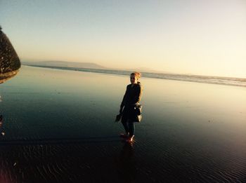 Portrait of woman standing at beach against clear sky