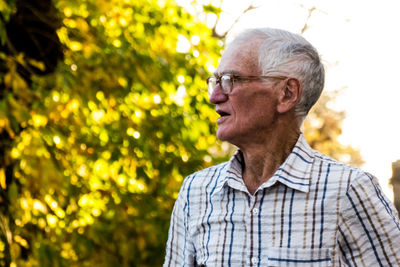 Senior man looking away while standing against trees
