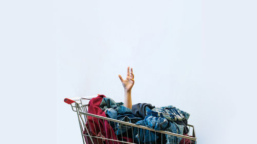 Cropped hand in shopping cart with laundry against white background
