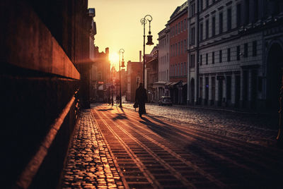 Rear view of man walking on footpath in city at sunset