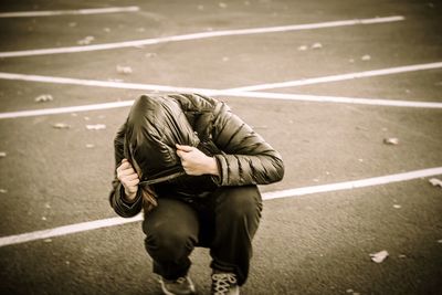 Girl wearing jacket while crouching on road