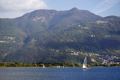 Sailboat sailing on sea by mountains against sky