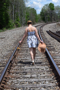Rear view of woman with hat walking on railroad track at forest