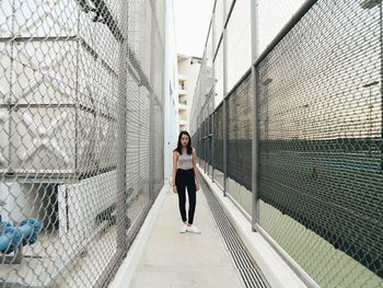 Full length portrait of woman standing on walkway amidst fence