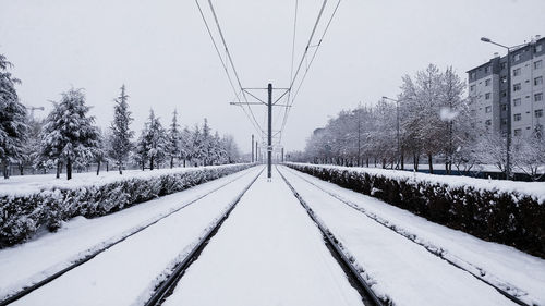 Snow covered railroad tracks by trees against sky