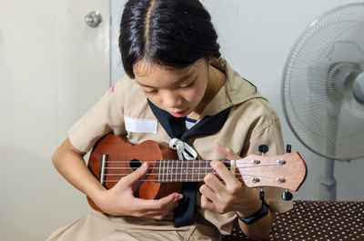 Girl playing small guitar while sitting at home