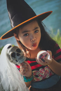 Portrait of girl wearing witch hat holding skull and crystal ball