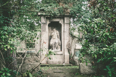 Statue amidst trees and plants against old building