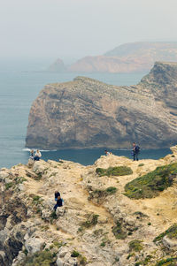 People on rock by sea against sky