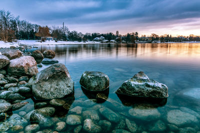 Rocks in lake against sky during sunset