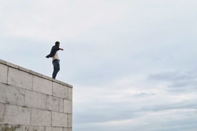 Low angle view of man standing on retaining wall against sky