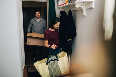 Couple carrying bag and box while moving in new house