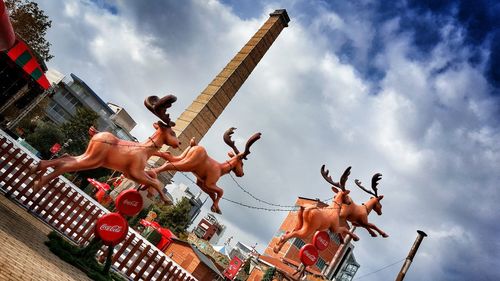 Reindeer sledge sculpture in city against cloudy sky