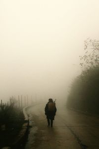 Rear view of man walking on snow covered landscape in foggy weather